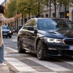 Woman raises her hand in frustration as a black BMW drives across a marked pedestrian crossing without yielding.