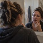 Middle-aged woman examining a gap from missing teeth while looking into a bathroom mirror.