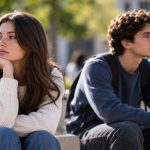 Young woman and man sitting apart outdoors, looking in opposite directions in a university setting.